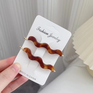 Detail of two tortoise shell acetate wavy hair clips on a white fashion jewelry card