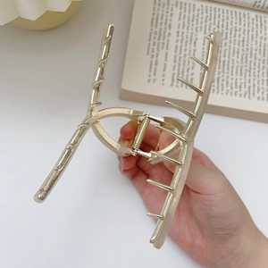 Detail of a large cream acetate hair claw clip with golden metal teeth held by hand