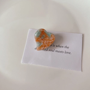Detailed macro view of heart-shaped acetate hair clip with orange and mint marble texture
