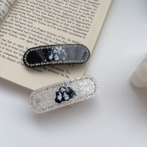 Detail of oval acetate hair clips with cat pattern and sparkling rhinestones on book