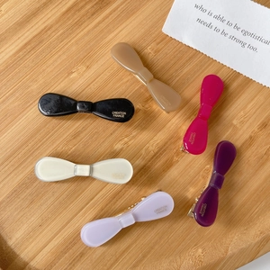 Set of six colorful bow-shaped acetate hair clips in various glossy finishes on wood