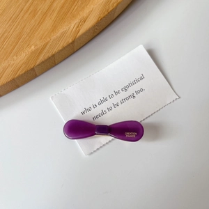 Detail view of purple acetate bow hair clip featuring golden Creation France logo text