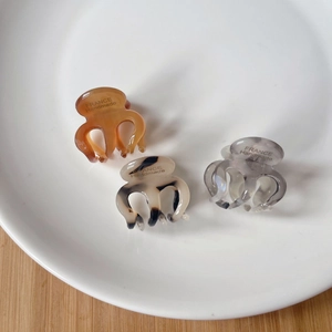 Three acetate mini claw clips in amber, marble, and grey patterns on a white porcelain plate