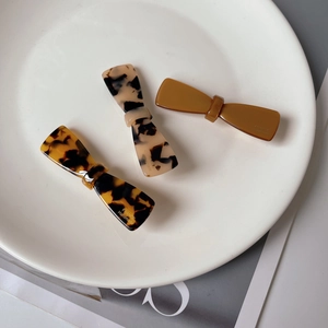 Three acetate bow hair clips in tortoiseshell and brown displayed on a ceramic tray