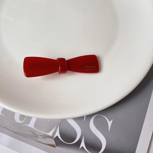 Detail of red handmade acetate bow hair clip with gold label on white ceramic plate