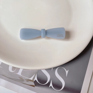 Detail of light blue bow hair clip with gold label on white ceramic plate