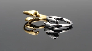 Detail view of gold and silver hugging hands rings with high-polished mirror finish