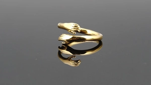 Macro detail of a polished golden embrace hand-shaped ring showing creative textures