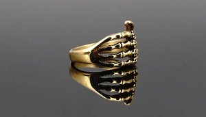 Detailansicht eines goldenen Punk-Totenkopf-Handrings auf reflektierendem Schwarz