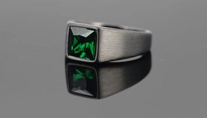 Detail of brushed dark grey metal ring featuring a square-cut green gemstone setting