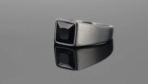 Macro detail of men's square signet ring with black gemstone and brushed metal finish
