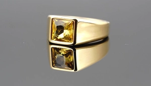 Macro shot of gold-plated signet ring with a square yellow gemstone on black reflection