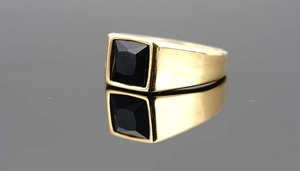 Macro detail of men's gold plated ring with square black gemstone and wide band