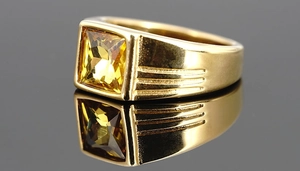 Detailansicht eines Goldrings mit quadratischem gelbem Edelstein und texturierter Ringschiene