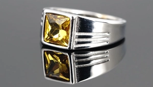Makroaufnahme eines Herrenrings aus Edelstahl mit quadratischem gelbem Edelstein auf Spiegel