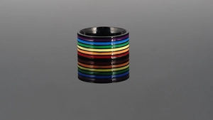 Makroaufnahme eines schwarzen Titanrings mit bunten Regenbogenstreifen auf reflektierender Fläche