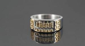 Macro detail of bicolored abacus ring with golden coin patterns and brushed steel finish
