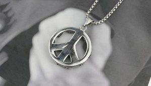 Detail of vintage silver peace sign pendant with box chain on a textured backdrop