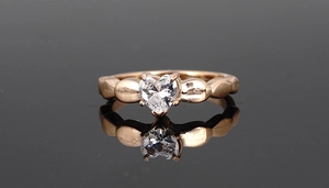 Macro view of rose gold ring with heart-cut zircon on a reflective black surface