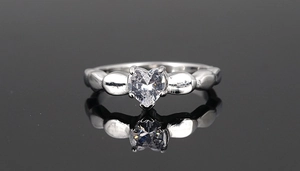 Detail view of heart-shaped crystal ring with silver setting on a dark mirror surface