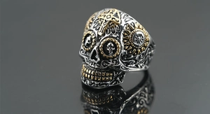 Makroaufnahme von Totenkopfring mit graviertem Kreuz und floralen Mustern in Gold-Silber