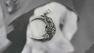 Detail of vintage silver crescent moon pendant with rose carvings and oxidized texture