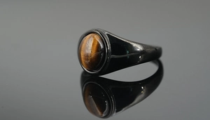 Macro detail of men's titanium signet ring with polished black band and round tiger eye stone