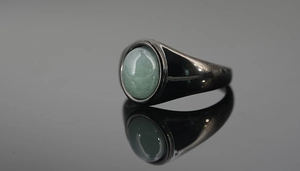 Macro side view of a black signet ring featuring a polished green cabochon gemstone