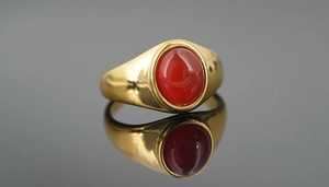Macro detail of a gold signet ring featuring a polished oval red agate stone setting