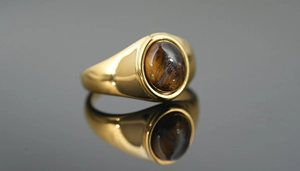 Macro shot of gold signet ring featuring a polished oval tiger eye stone with reflections