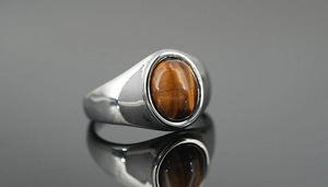 Macro detail of a polished titanium steel ring featuring an oval tiger eye stone inlay