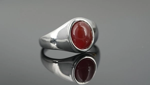 Macro shot of a silver signet ring with an oval red agate stone on a black mirror surface