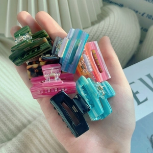 Mini acetate hair claw clips in various marble and striped colors with gold letter accents