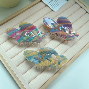 Three colorful acrylic butterfly hair claws with vibrant stripes on a velvet display tray