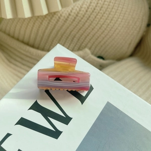 Detail view of mini acetate hair claw with pink marble texture and gold lettering