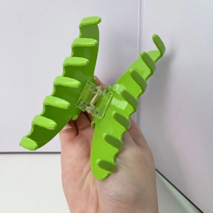 Close-up of a large neon green hair claw clip held by hand against a white background