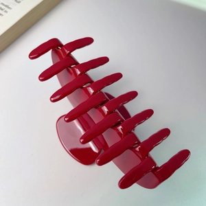 Glossy large red acetate hair claw clip with multi-tooth design on a neutral background