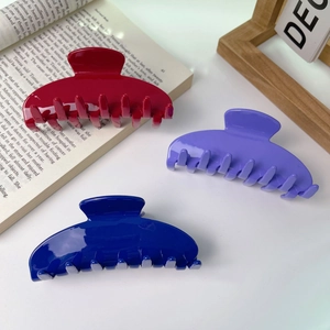 Three large acrylic shark hair clips in red, purple and blue displayed on a book background