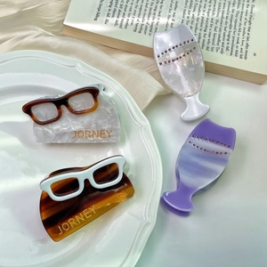 Detail view of acetate wine glass hair claws and chic eyewear clips on a ceramic plate