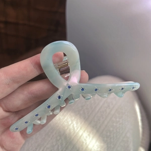 Close-up of light blue acetate hair claw clip with dark blue rhinestone accents
