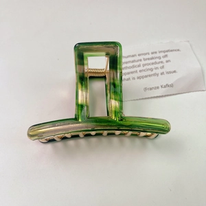 Minimalist green acetate hair claw clip with golden metal spring on a white background