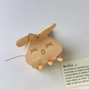 Gros plan d'une pince à cheveux lapin en acétate beige avec détails faciaux dorés