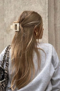 Détail d'une pince à cheveux marbrée beige et de créoles dorées sur un mannequin