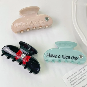 Three acetate hair claws in pink, black with bow, and blue with 'Have a nice day' text