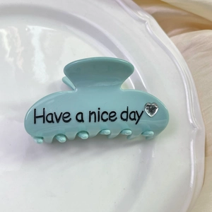 Macro shot of mint green acetate hair claw clip featuring black Have a nice day lettering