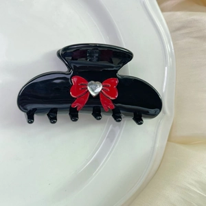 Close-up of black acetate hair claw with a red bow and heart-shaped rhinestone
