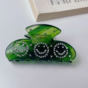 Close-up of translucent dark green hair claw clip with sparkling rhinestone smiley faces