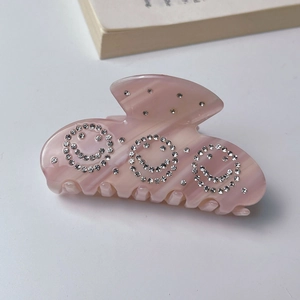 Close-up of pink marble acetate hair claw clip featuring three sparkling rhinestone smileys