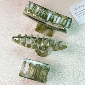 Three olive green marble acetate hair claws set on a minimalist textured background