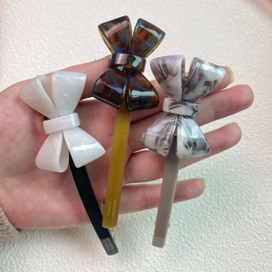 Three acetate bow hair clips in white, amber, and marble finishes with handmade detail